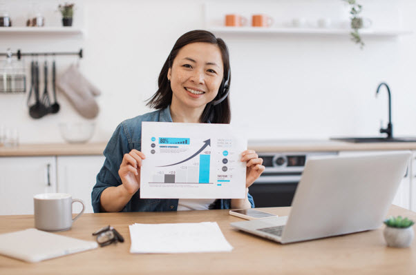 Woman Holding a Paper with Graph and a Laptop