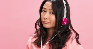 Upset confused Asian student young lady in pink hoodie sweatshirt with cute headphones looks at you posing isolated on over pink studio background. Good offer. Sound streaming platform ad concept