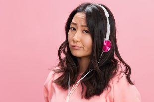 Upset confused Asian student young lady in pink hoodie sweatshirt with cute headphones looks at you posing isolated on over pink studio background. Good offer. Sound streaming platform ad concept