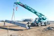 A crane lifting slabs guided by two people