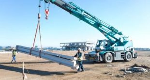 A crane lifting slabs guided by two people