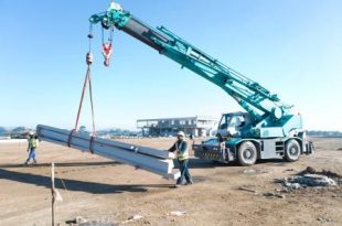 A crane lifting slabs guided by two people