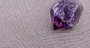 A deep purple amethyst crystal point resting on sand, demonstrating a natural method for grounding and charging crystal energy.