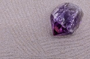 A deep purple amethyst crystal point resting on sand, demonstrating a natural method for grounding and charging crystal energy.