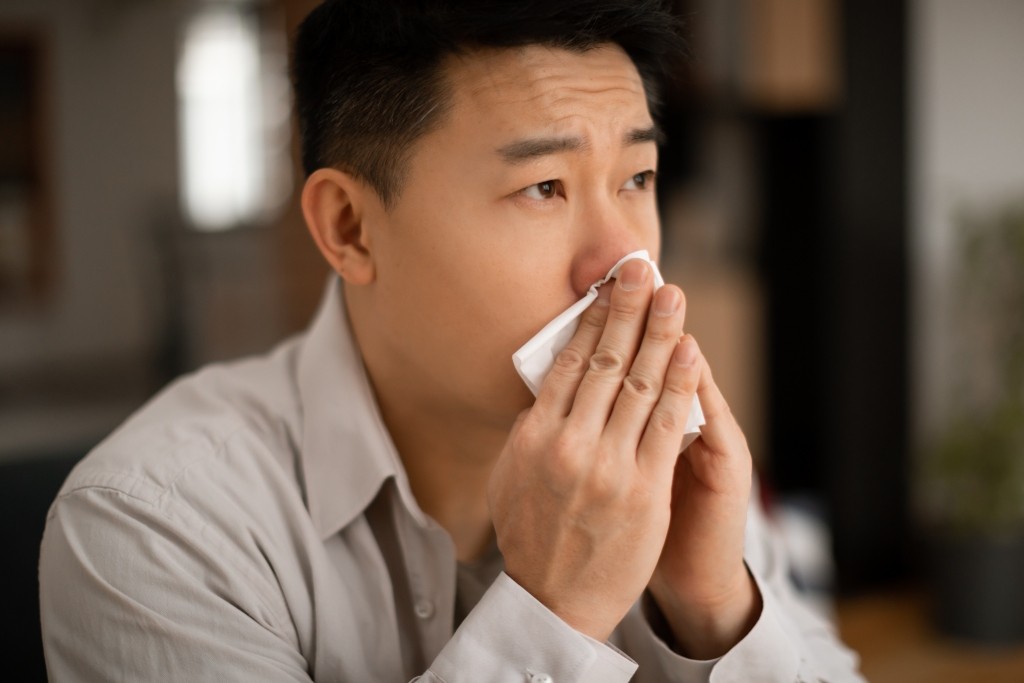 Allergic Rhinitis Symptoms Man with a runny nose blowing into a tissue, a common allergic rhinitis symptom